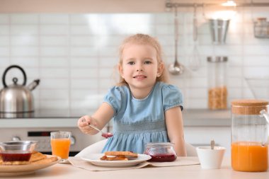 Sevimli küçük kız reçel mutfak masasında lezzetli kızarmış ekmek üzerine yayılıyor