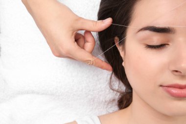 Young woman having professional eyebrow correction procedure in beauty salon, closeup clipart