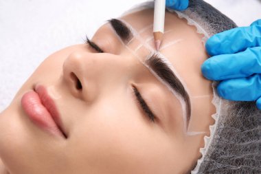 Cosmetologist preparing young woman for eyebrow permanent makeup procedure, closeup clipart