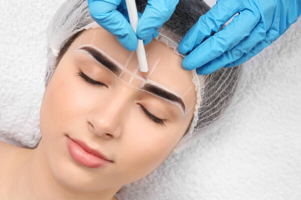 Косметолог готовит молодую женщину к процедуре макияжа бровей, крупным планом
