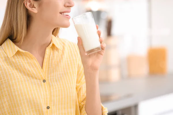 Beautiful young woman drinking milk in kitchen