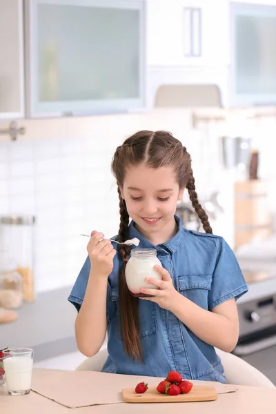 かわいい女の子のキッチンのテーブルでおいしいヨーグルトを食べて — ストック写真