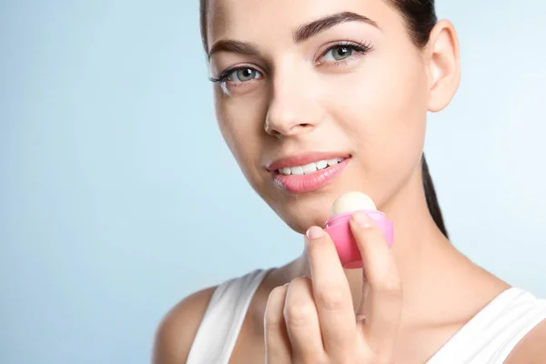 Giovane Donna Che Applica Balsamo Sulle Labbra Contro Sfondo Colore — Foto Stock