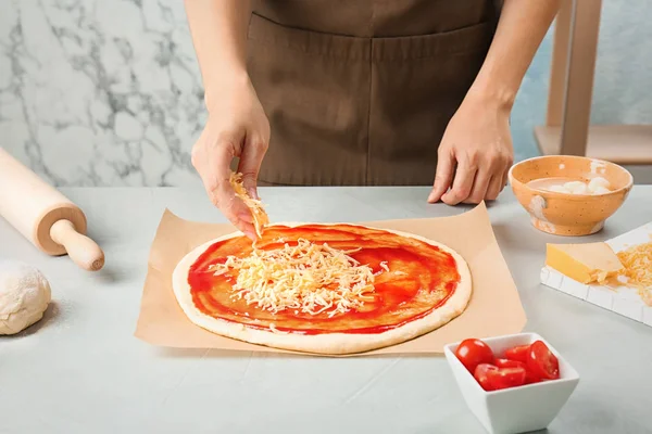 Woman adding cheese to pizza on table