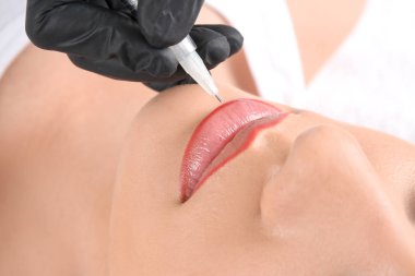 Young woman getting permanent makeup on lips in beautician salon, closeup clipart