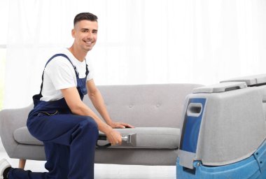 Kuru temizleme işçisi kanepedeki kiri temizliyor.