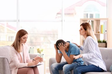 Genç çocuk ve annesi ofiste çalışan genç kadın psikolog