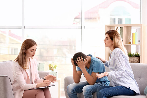Young female psychologist working with teenage boy and his mother in office