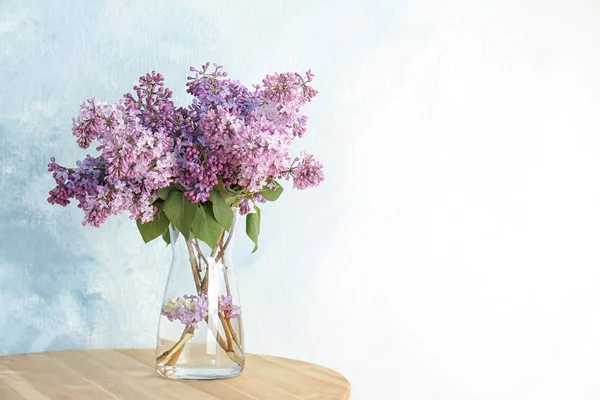 Vase with beautiful blossoming lilac on table against light background. Spring flowers