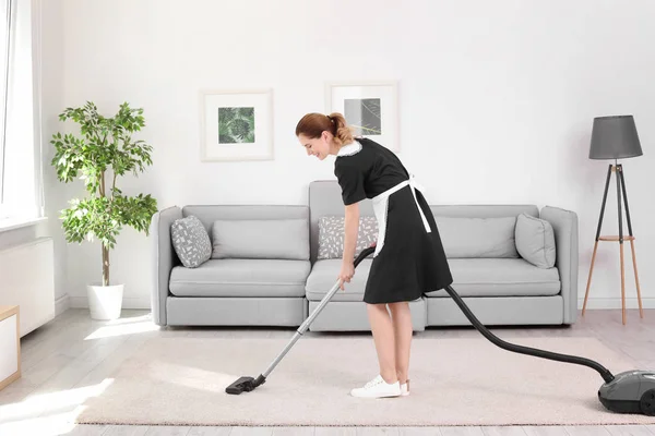 Female worker removing dirt from carpet with professional vacuum cleaner indoors