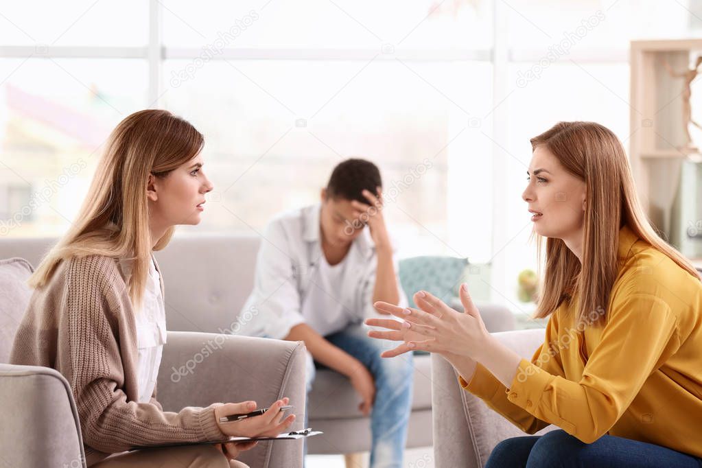 Young female psychologist working with teenage boy and his mother in office