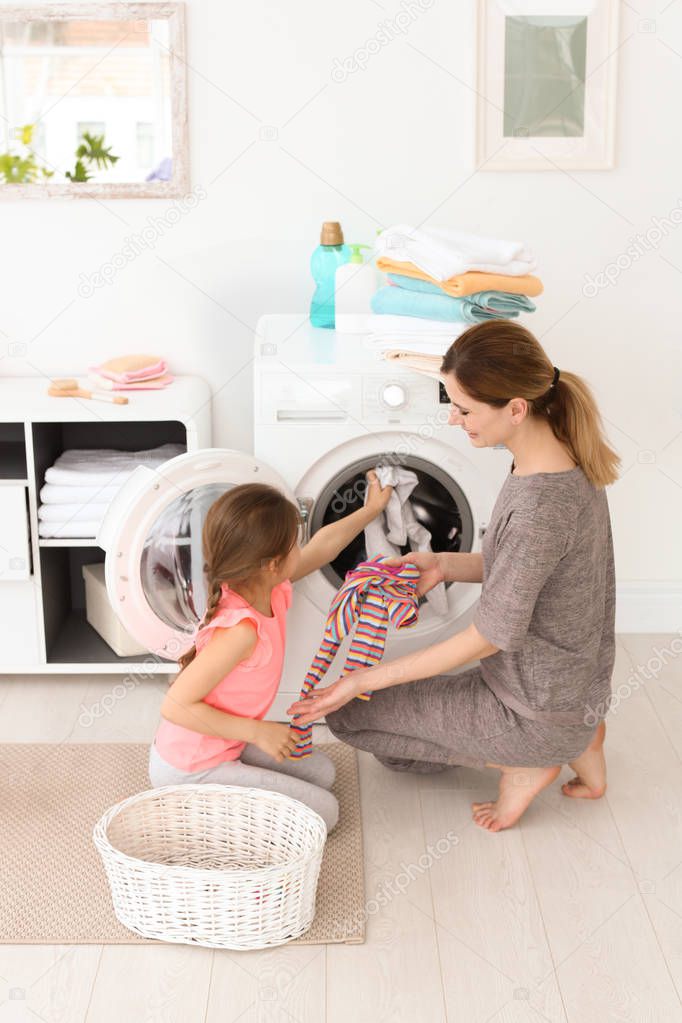 Housewife with little daughter doing laundry at home