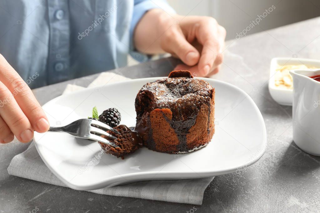 Woman eating delicious fresh fondant with hot chocolate at table. Lava cake recipe