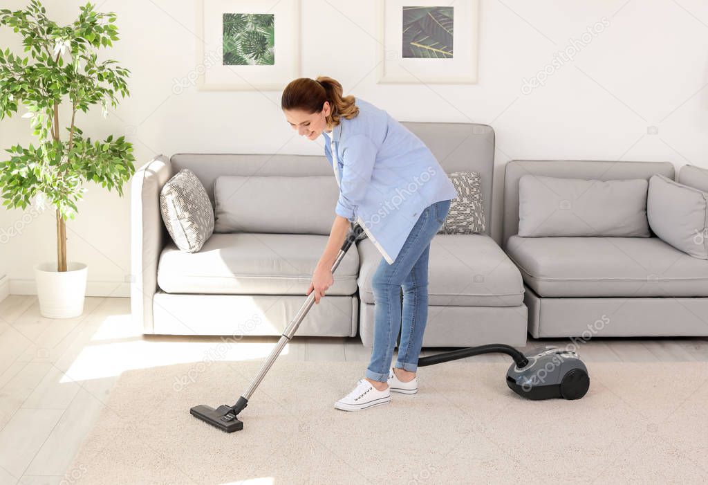 Woman removing dirt from carpet with vacuum cleaner at home