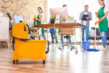 Kova ıslak zemin işareti ve profesyonel kapıcı üniformalı ofis temizlik ekibi ile paspas