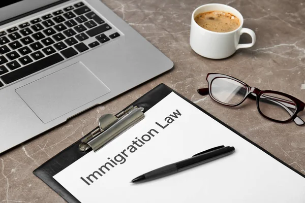 Clipboard with words IMMIGRATION LAW and laptop on table, closeup