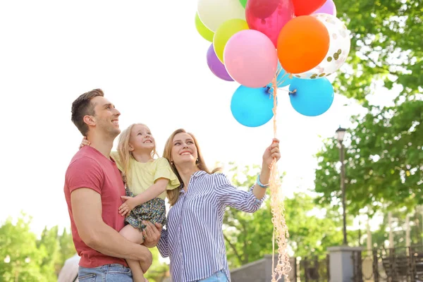 Happy family with colorful balloons outdoors on sunny day