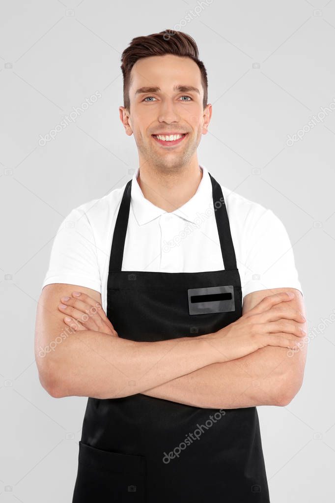 Portrait of handsome waiter in apron on light background