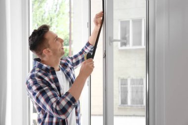 Genç adam mühürleme köpük bandı pencere kapalı koyarak
