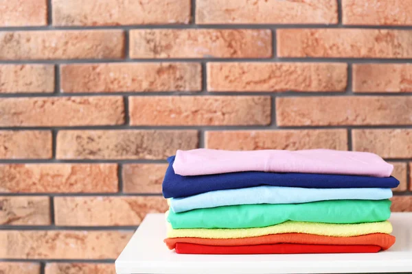 Stack of rainbow clothes on table against brick wall background