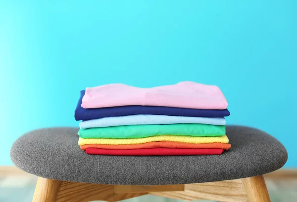 Stack of rainbow clothes on stool against color background