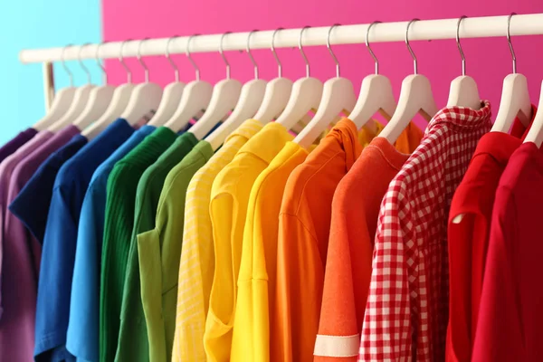 Rack with rainbow clothes on color background