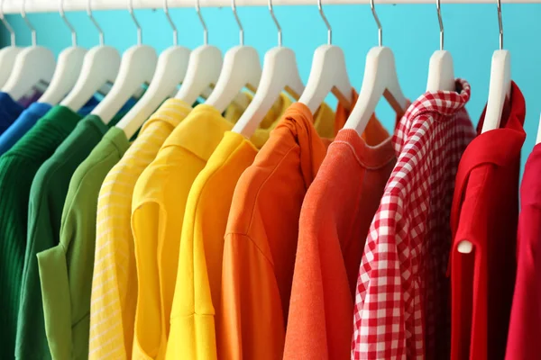 Rack with rainbow clothes on color background