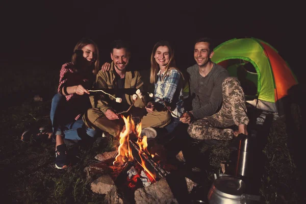 Friends frying marshmallows on bonfire at night. Camping season