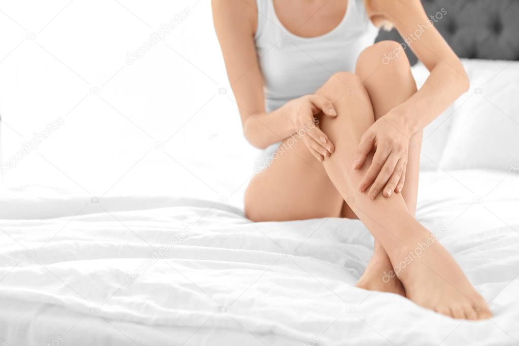 Young woman showing smooth silky skin after epilation on bed at home