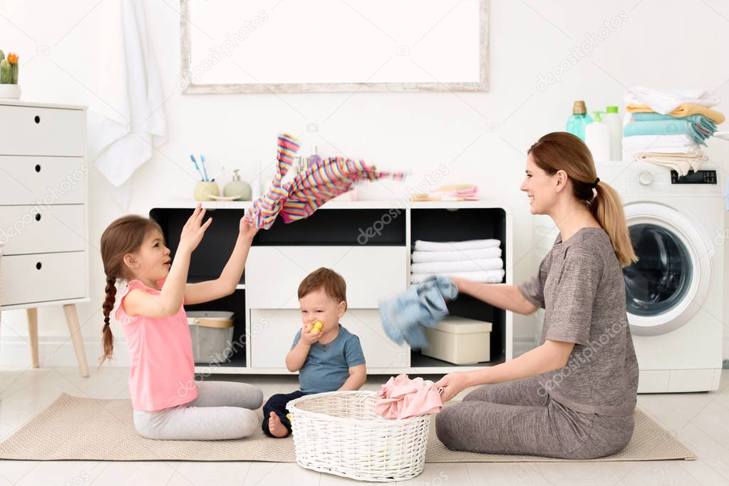 Housewife and children having fun while folding freshly washed clothes in laundry room