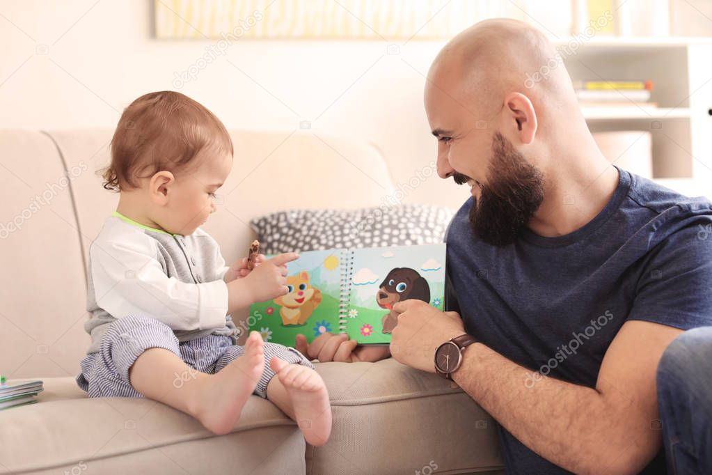 Dad reading book with his little son in living room