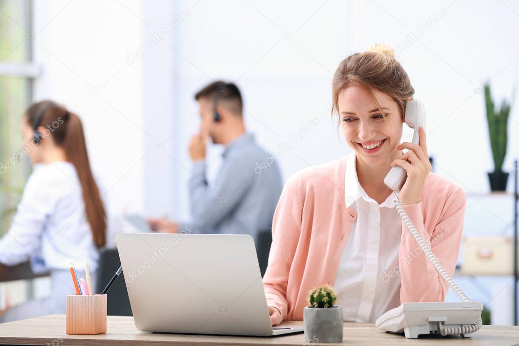 Female receptionist talking on phone at desk in office