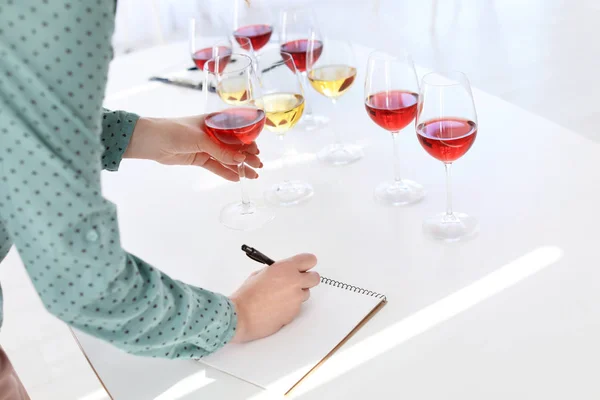 Woman with notebook tasting delicious wine at table indoors