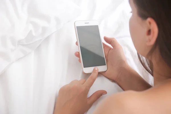 手持手机空白屏幕的年轻女子在手上的床上 — 图库照片