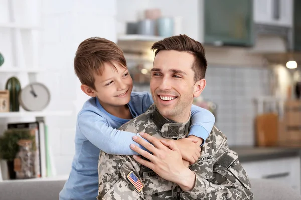 Young man in military uniform with his little son at home