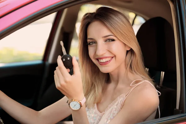 Beautiful young woman with key sitting in car