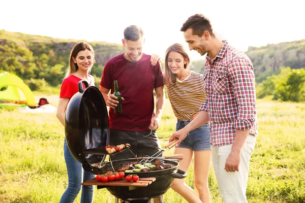 Young people having barbecue in wilderness. Camping season