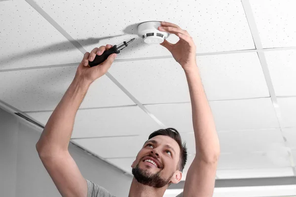 Male technician installing smoke alarm system indoors