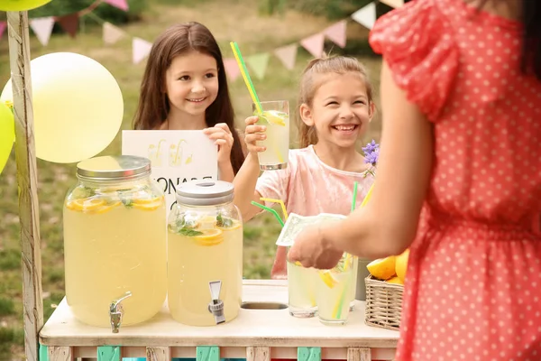 小女孩卖天然柠檬水给妇女在公园的立场 — 图库照片
