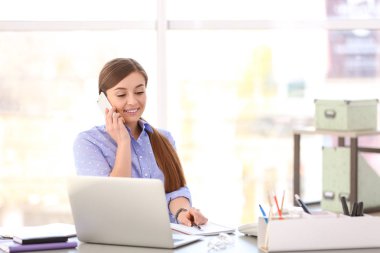 İş yerinde telefonla konuşan genç bir kadın.