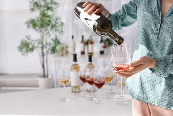 Woman pouring tasty wine into glass indoors