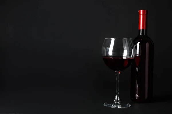 Bottle and glass of expensive red wine on dark background