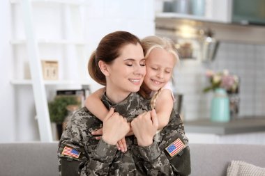 Woman in military uniform with her little daughter at home clipart