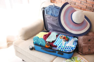 Açık bavul farklı kıyafetler ve aksesuarlar kanepe kapalı. Tatil için ambalaj