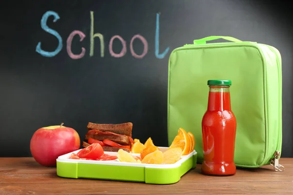 Appetizing food in lunch box and bag on table near chalkboard with word SCHOOL