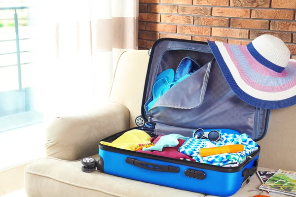 Open suitcase with different clothes and accessories on sofa indoors. Packing for vacation