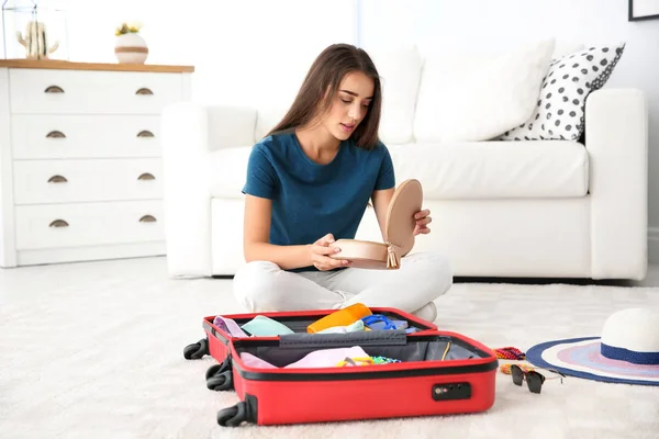 Young woman packing suitcase for summer journey at home