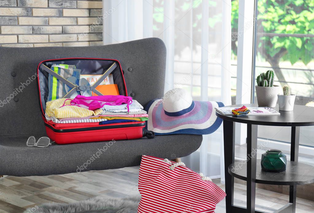 Open suitcase with different clothes and accessories on sofa indoors. Packing for vacation