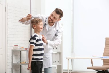 Doctor measuring little boy's height in hospital clipart