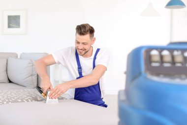 Kuru temizleme işçisi kanepedeki kiri temizliyor.